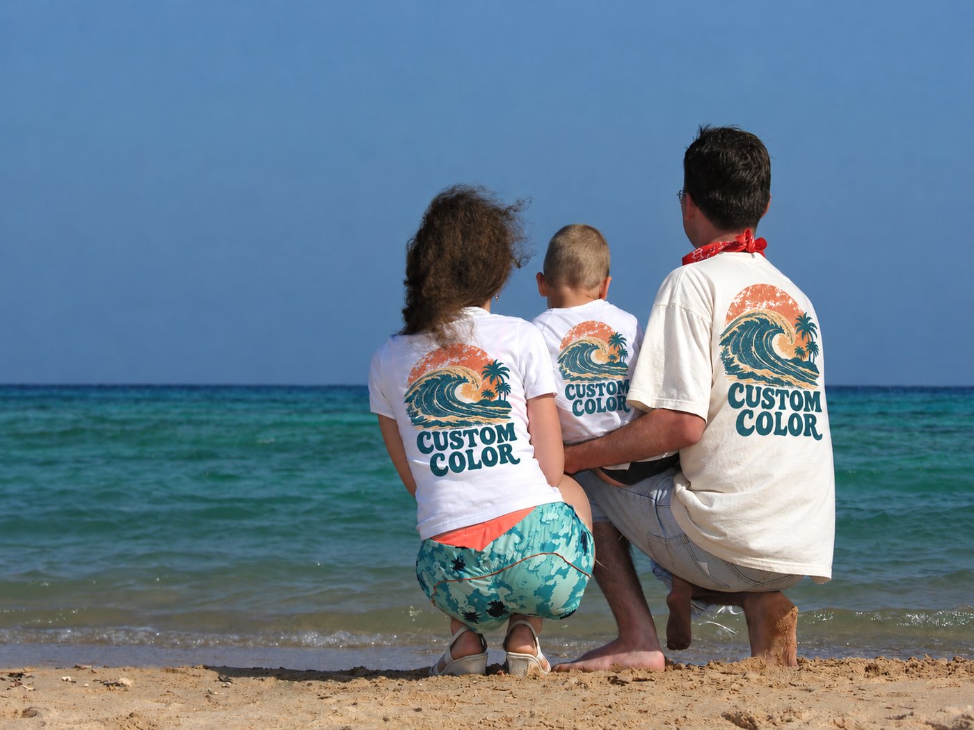 Family of three at the shoreline seen from behind, their white tees printed with the Custom Color logo