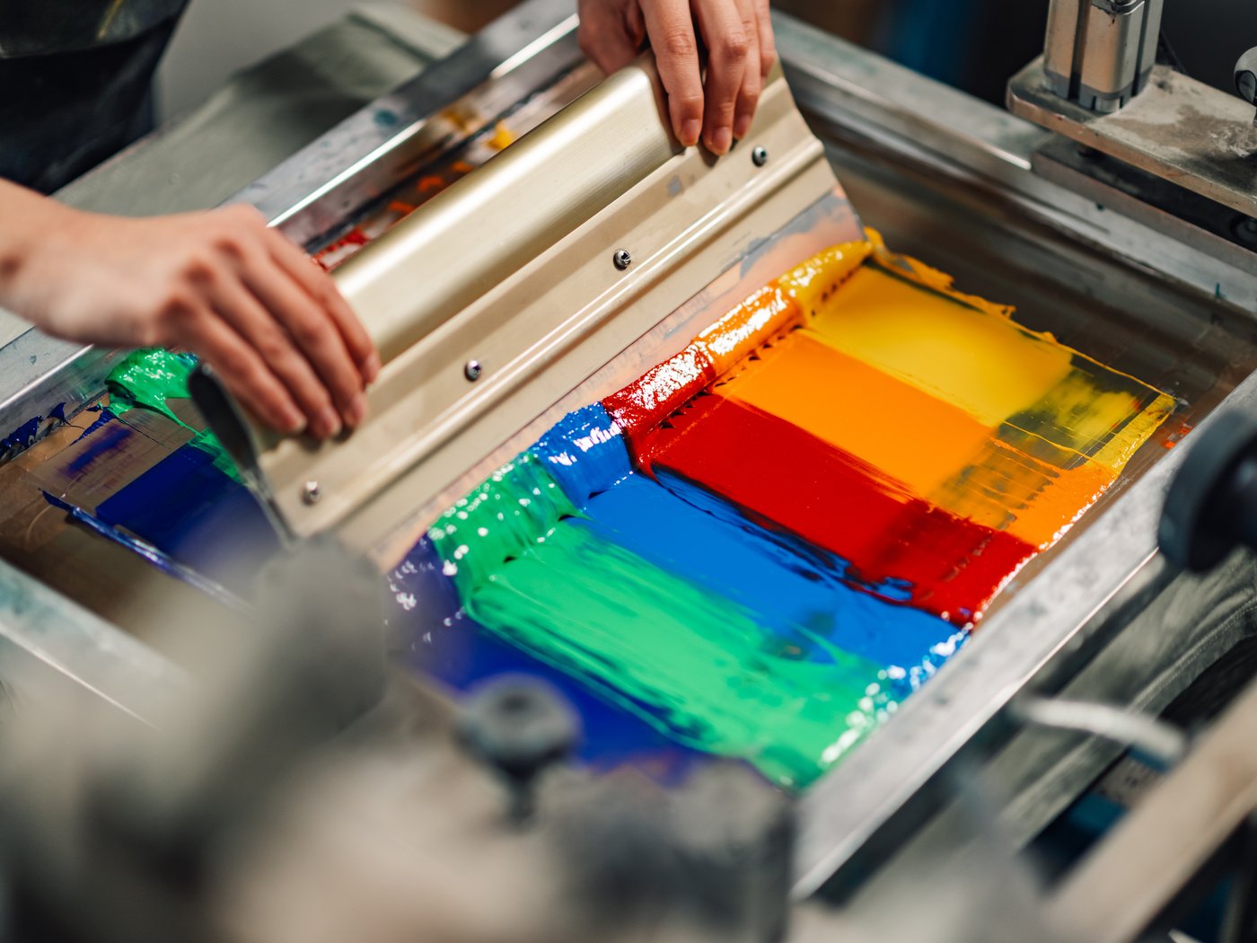 Squeegee pulling red, yellow, green and blue ink across a screen