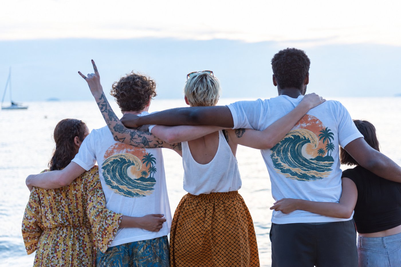 Friends at sunset with their backs to the ocean, two of them in tees with a printed wave design