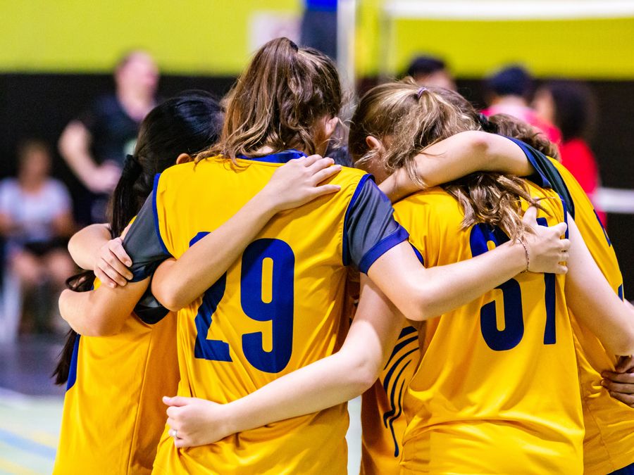 Girls volleyball team in yellow jerseys huddling together in a gym