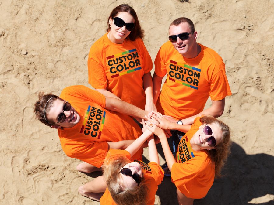 Five volunteers in matching orange tees stacking hands on the sand